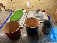 Photo of various serveware items including 2 pottery vases, rectangular serving trays in white and green, a white dish with a metal insert