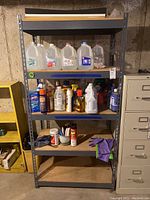 Front view of the metal shelving unit showing four particle board shelves with various items on the shelves (not included in lot).