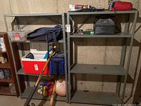 Two gray metal shelving units in basement setting, some shelves holding various packed items, showing general wear and need for cleaning.