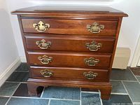 Front view of wooden side table showing four drawers with brass pulls and visible surface wear.
