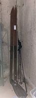 Pair of vintage wooden skis with fishing rods and single black diving flipper standing against wall.