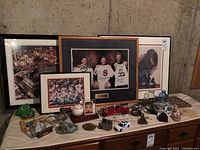 Full view of the table showing a collection of framed sports photos, animal figurines, toy cars, decorative stones, and other collectibles.