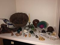 Overview photo of the statuettes laid out on a shelf, various animals including birds, alligator, turtles, bear, and others visible alongside a wicker basket with pine cones and a candle in holder.
