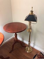 Photo showing wooden pedestal table and brass floor lamp side-by-side.