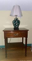 Full view of Stickley wooden side table with drawer and ceramic base lamp with shade on top