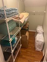 Shelving with neatly folded towels, blankets, and a woven basket below. Cardboard box on floor along wall.