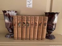 Two swirled glass vases with the eight Mother West Wind books lined up between them on a shelf.