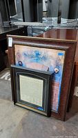 Two framed prints leaning against each other and a table, including a large 'We The People' print with a reddish-brown frame and a smaller black-framed Declaration of Independence copy.