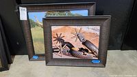 Three pieces of framed western-themed wall art including two prints showing metal western spurs and one Texas Longhorn print, frames are textured and dark brown, placed on floor.