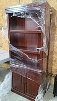 Full view of laminate wood bookcase partially wrapped in plastic.