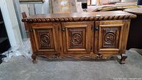 Front view of wood console table with three carved Texas star doors, carved top edge, and cabriole legs.