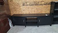 Full view of black laminate console cabinet against an OSB wooden wall, shows overall shape and design with doors closed.