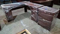 Wide view of the wrapped three-piece office furniture set showing the two-piece L-shaped desk and file cabinet together.