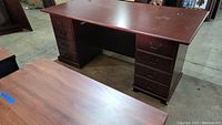 Dark wood tone executive laminate desk with two drawer pedestals showing scratches and damage on the surface.