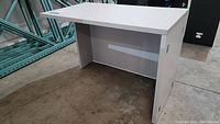 Full view of white laminate desk with flat top and modesty panel on the concrete floor in warehouse setting.