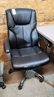 Front view of the black adjustable rolling desk chair showing its overall shape, padded armrests, and swivel base.