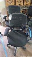 Front view of one black mesh-back office chair with padded seat and adjustable armrests, showing the base and caster wheels.
