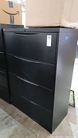 Front view of black filing cabinet with four drawers showing handles and unit size label.