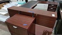L-shaped office desk, overhead hutch, and file cabinet seen from an angled side view showing the dark laminate finish and condition with laminate peeling and scratches.