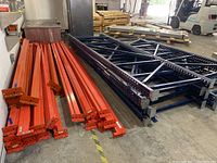 Stacked orange cross beams beside blue upright supports on warehouse floor