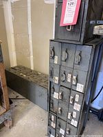 Photo showing two stacking metal storage drawer units with labels on drawers, placed in corner next to wall.