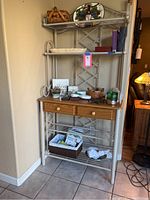 Photo of metal and wood baker's rack showing overall structure and contents on shelves including trays, a basket, decorative items, book, and candle.