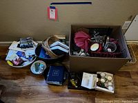 Box and plates filled with barware tools, books, and candles on floor