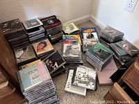 Multiple stacks of CDs on the floor showing a large collection spread out with some titles and artists visible.