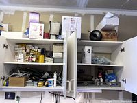 Wide view of open cupboards with assorted hardware items including boxes, electrical supplies, hand tools, and other miscellaneous items.