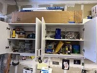 Two white cupboards with various hardware and supplies inside them.