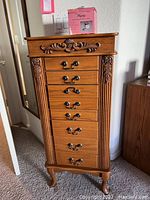 Full front view of the wooden jewelry cabinet showing eight drawers and carved detailing.