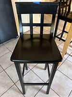 Front view of black wooden kitchen stool showing square seat and open backrest with grid slats.