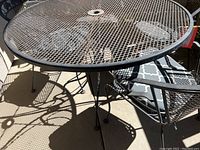 Photo of black metal round mesh patio table with umbrella hole showing shadows on concrete patio floor.