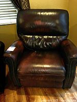 Front view of the oversized dark brown leather recliner chair with visible wear on cushion