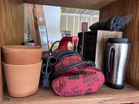 Photo showing two terracotta clay planters, Red Devil hand vacuum with fabric cover, travel mug, and other miscellaneous items on wooden shelf.