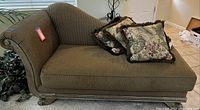 Striped upholstered settee with carved wooden legs and three floral accent pillows arranged on the seating surface.