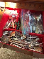 Drawer containing an assortment of spoons, forks, ladles, and serving utensils of silverplate and stainless steel in mixed patterns.