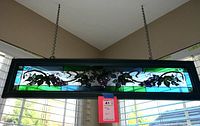 Frontal image showing entire rectangular stained glass panel with grape vine design hanging by metal chains.