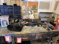 Wide view of workbench surface showing metal toolbox filled with assorted hand tools, Sony portable stereo, and metal ashtray among other items.