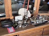 Wide view of desk surface showing watches, bracelets, candlesticks with red candles, trinket tray, and Salton clock radio.