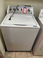 Full view of white Whirlpool top load washer with closed lid and plugged power cord on top.