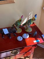 Two colorful ceramic cockatoos, small white porcelain birds, wooden bull, and wooden donkey on a red table.