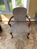 Front view of the wood armchair with leopard print upholstery, showing the legs, arms, and cushioned seat.