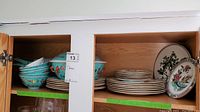 Overall cabinet view: turquoise bowls left, matching tureen, stacked white plates and two decorative service plates right.