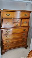 Full view of vintage wooden dresser showing all nine drawers and brass handles, standing on short carved legs.