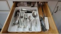Drawer with assorted Retroneu flatware forks, spoons, and knives organized in a white plastic flatware tray, plus various kitchen utensils behind.