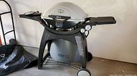 Frontal image of the Weber Q 320 grill showing the white lid with temperature gauge and black side shelves in folded position with wheels on base.