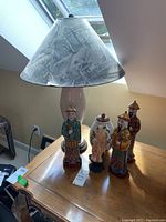 Table lamp on a wooden table with four ceramic statuettes in front and a painted vase.