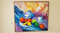 Full view of the oil on canvas still life painting showing fruit, blue and white ceramic container, and cup on colorful background.