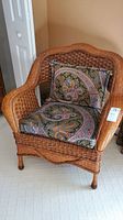 Front view of rattan arm chair with visible removable seat cushion and back pillow in paisley pattern.